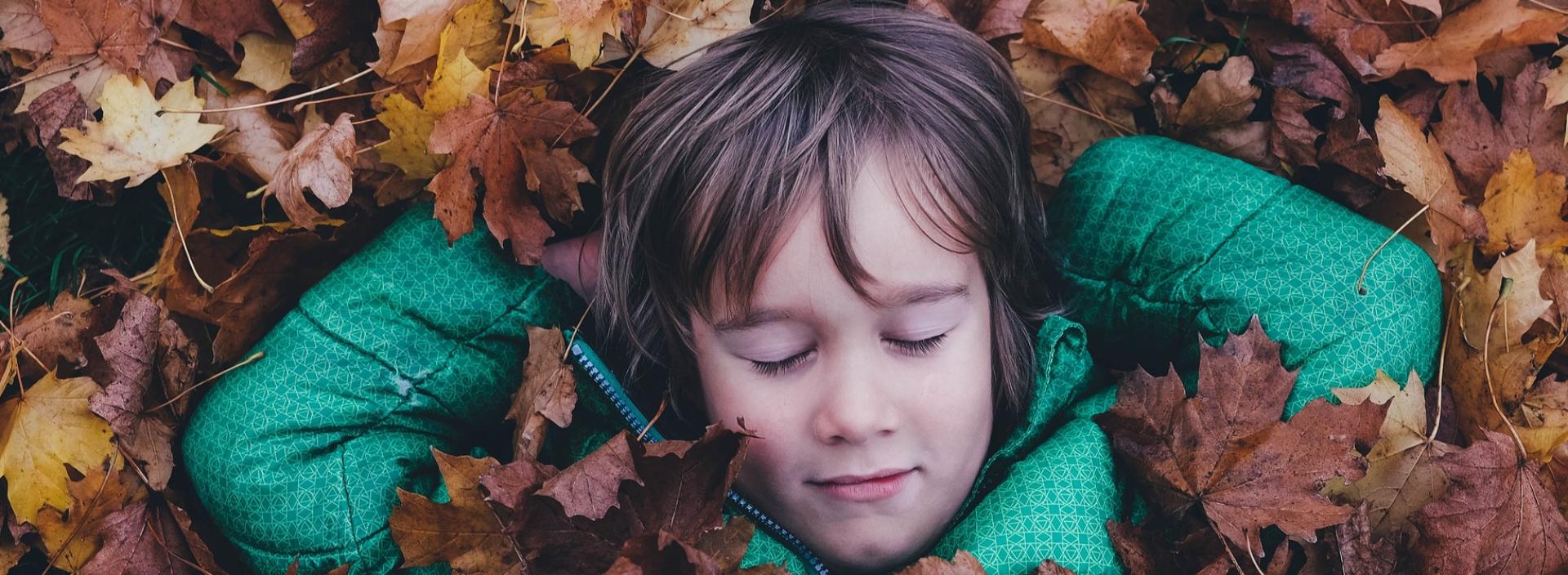 Kind im Herbstlaub liegend