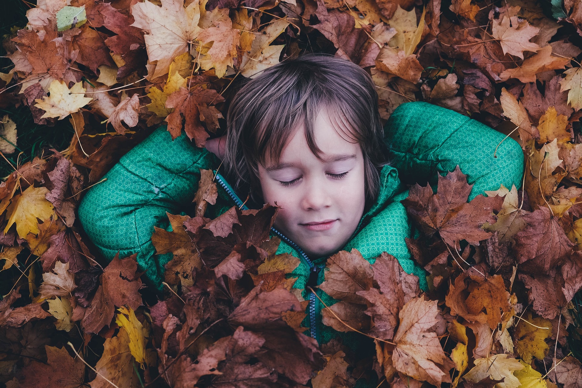 Kind im Herbstlaub liegend