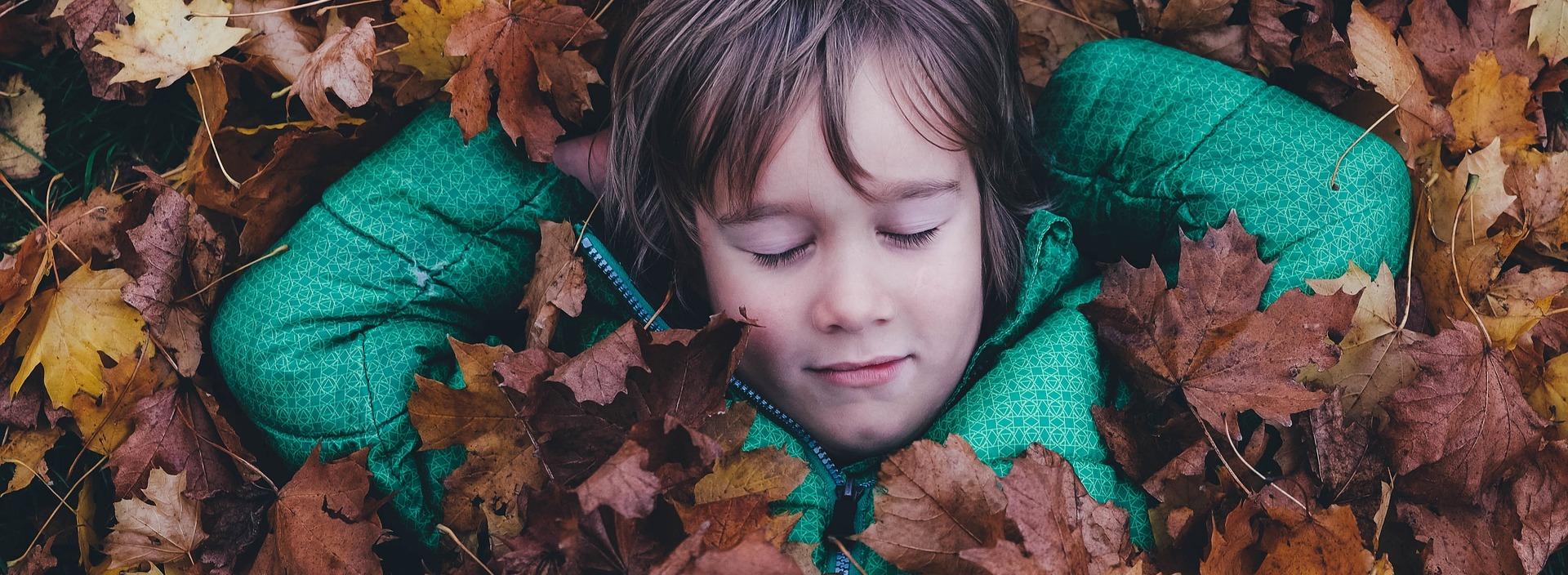 Kind im Herbstlaub liegend