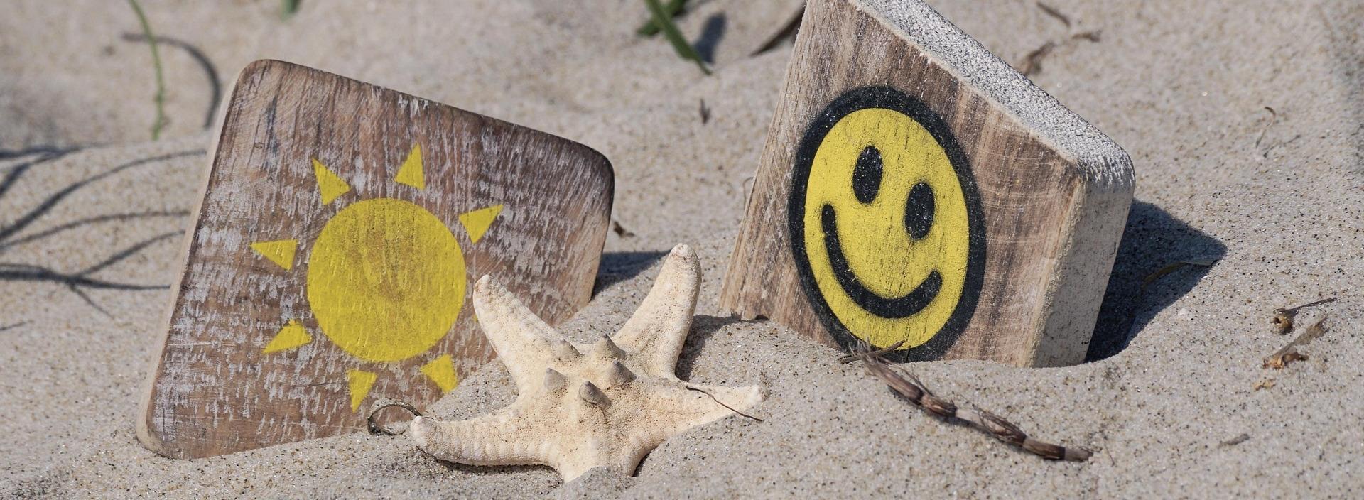 Holzplättchen mit Sonne und Smiley sowie ein Seestern im Sand.