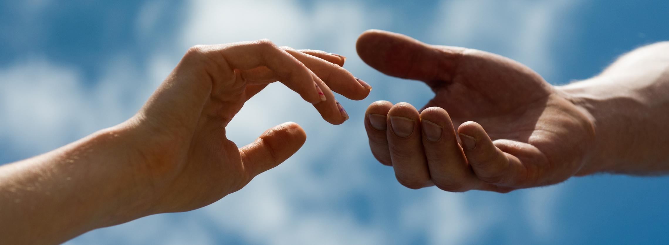 Die Hand eines Mannes, die dieser unterstützend hinhält, und die einer Frau, kurz vor dem Zufassen.