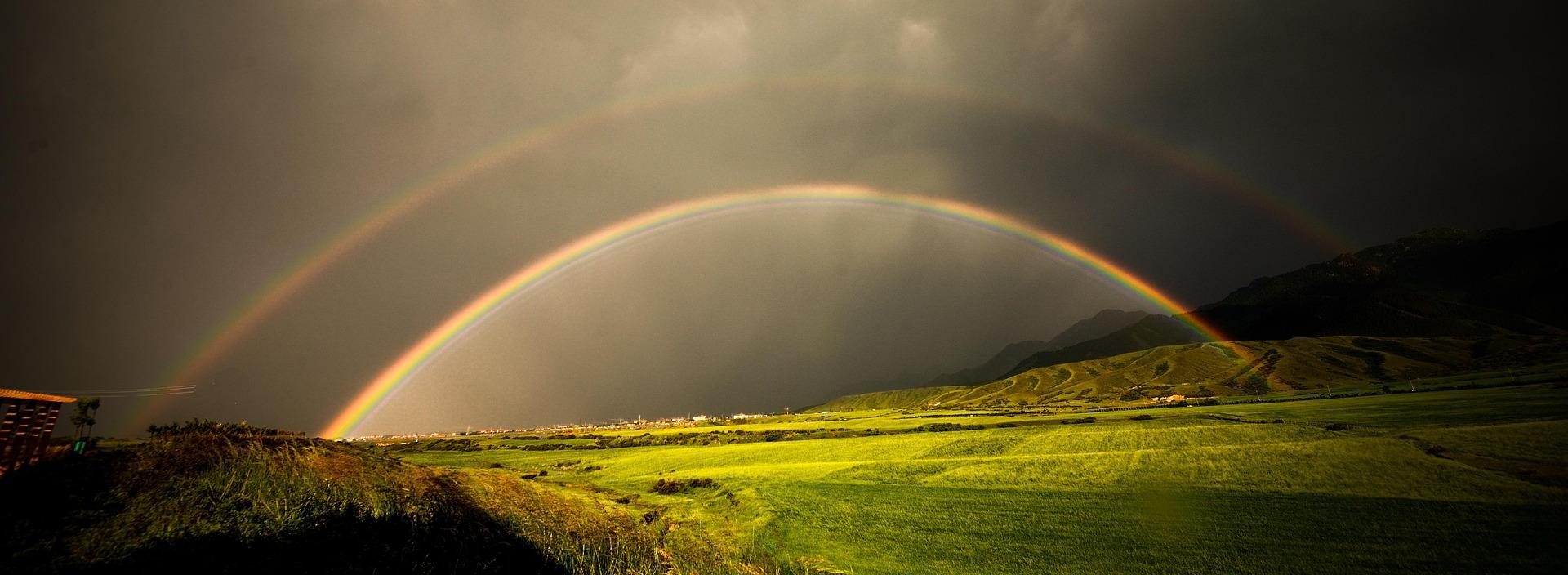doppelter Regenbogen über grünem Feld bei stürmischem Wetter
