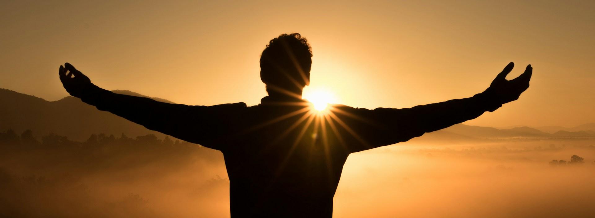 Silhouettenfoto eines Mannes auf einer Klippe während des Sonnenuntergangs