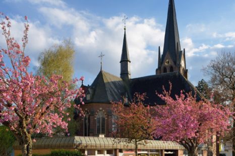 Außenansicht von St. Johannes Baptist im Frühling mit rosa blühenden Bäumen