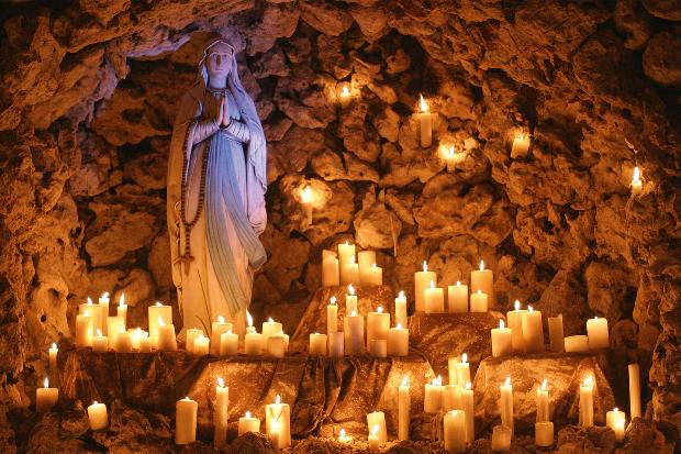 Marienstatue in einer Grotte mit vielen brennenden Kerzen drumherum