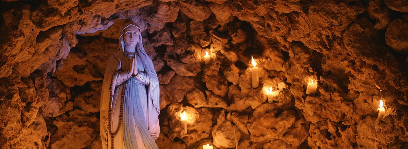 Marienstatue in einer Grotte mit vielen brennenden Kerzen drumherum