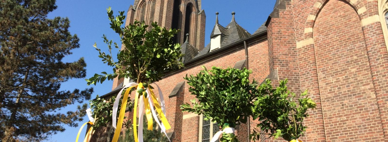 Stöcke mit Buchsbaumsträussen und Bändern vor St. Johannes Baptist