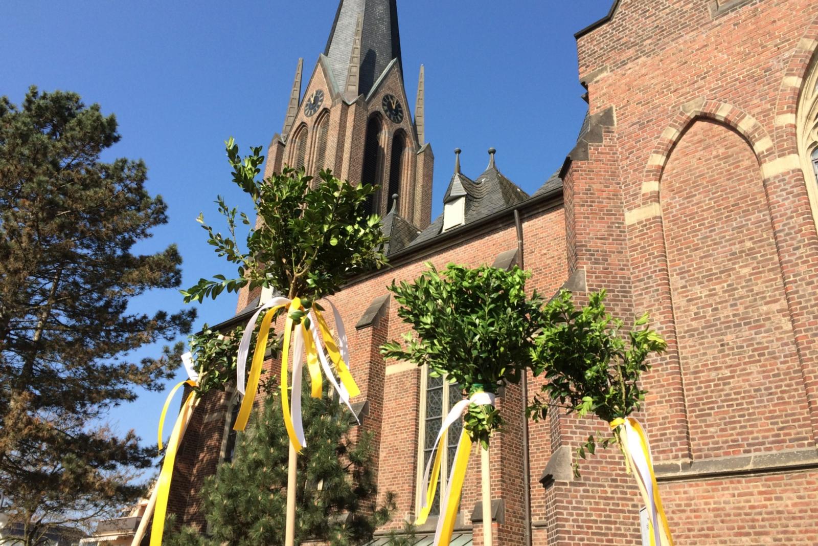 Stöcke mit Buchsbaumsträussen und Bändern vor St. Johannes Baptist