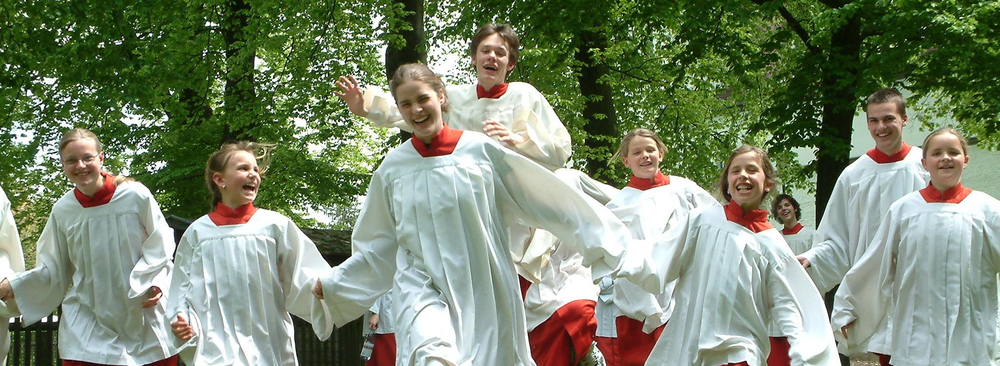 Mehrere Ministranten in roten-weißen Gewändern laufen lachend über eine Wiese.
