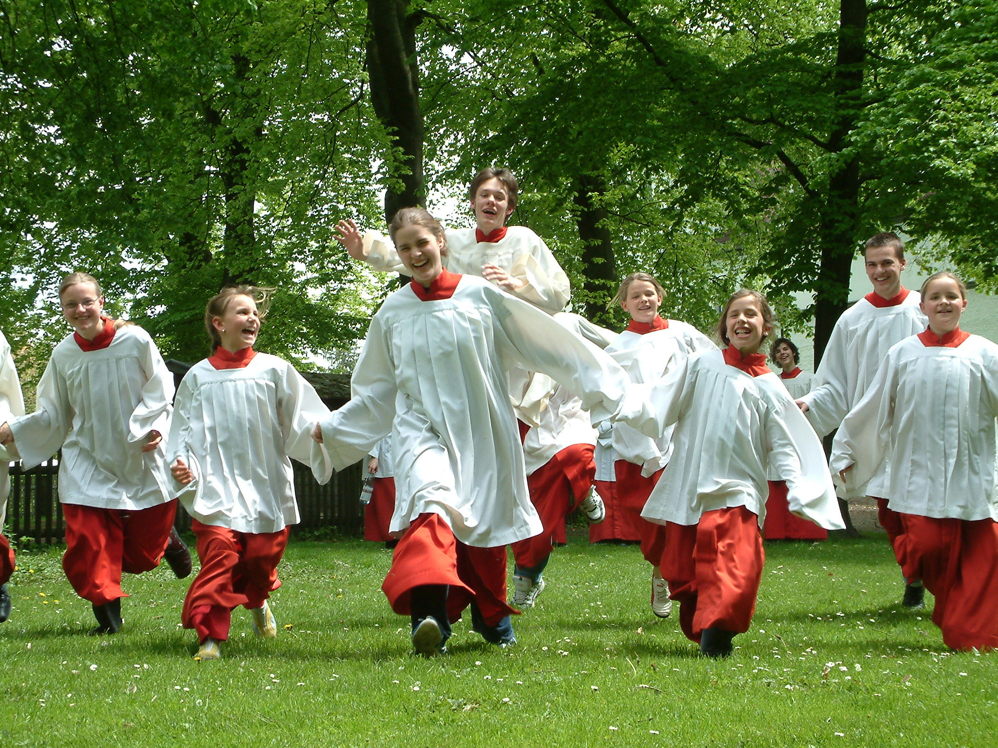Mehrere Ministranten in roten-weißen Gewändern laufen lachend über eine Wiese.