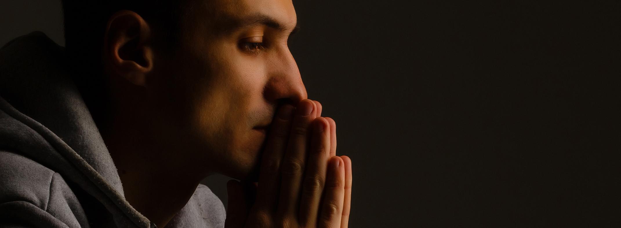 religiöser junger Mann, der zu Gott betet - schwarzer Hintergrund