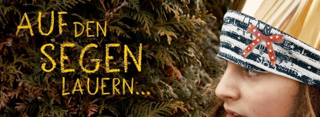 Sternsingerin, die hinter einer Hecke hervorguckt mit Schriftzug 'Auf den Segen lauern'
