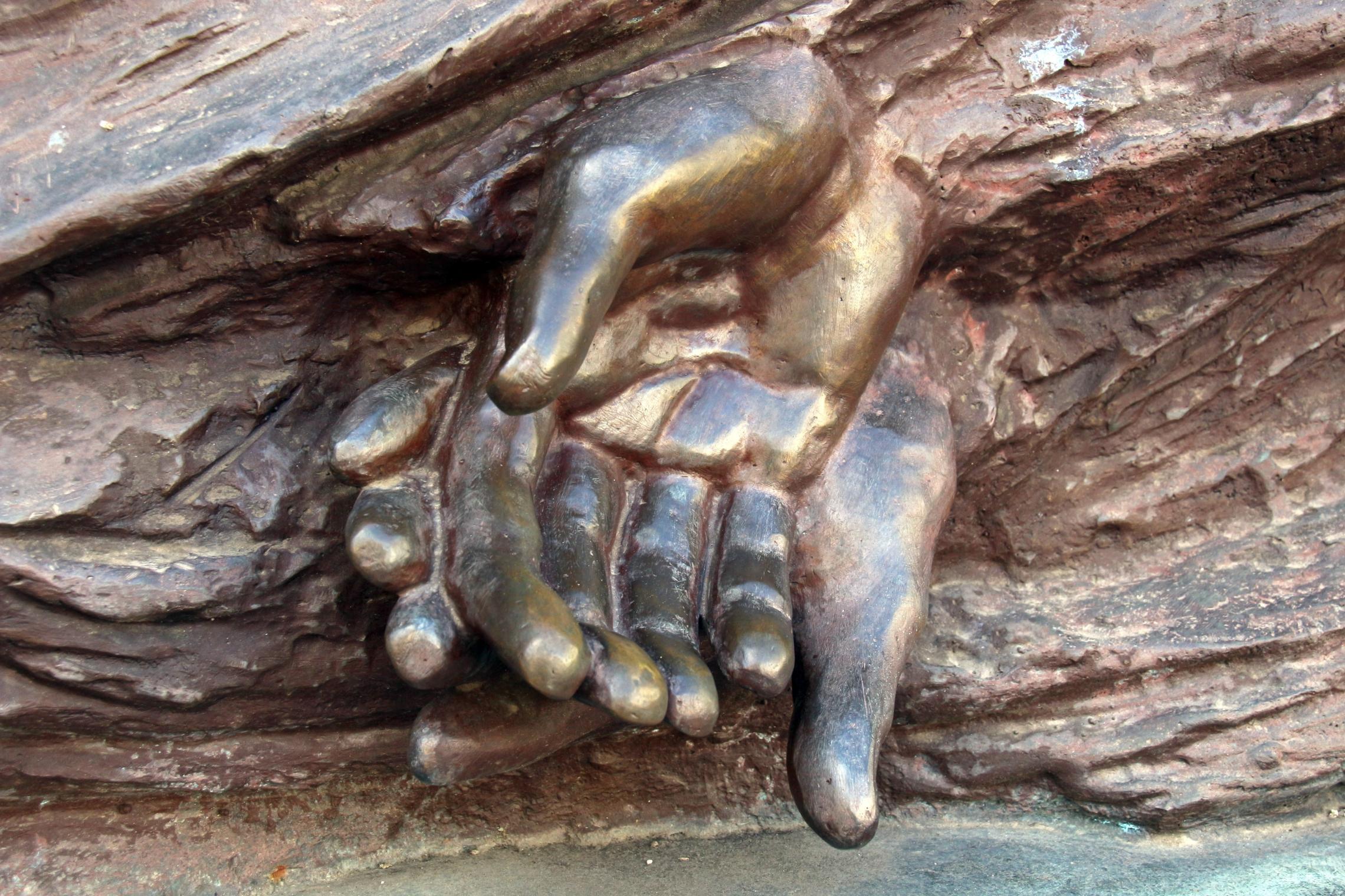 2 offen ineinanderleigende Hände; Detail eines Tiefenreliefs von Hélder Carvalho, Denkmal zum 500-jährigen Jubiläum der Misericórdia de Braga, 2013, an der Außenseite der Kathedrale von Braga, Portugal.