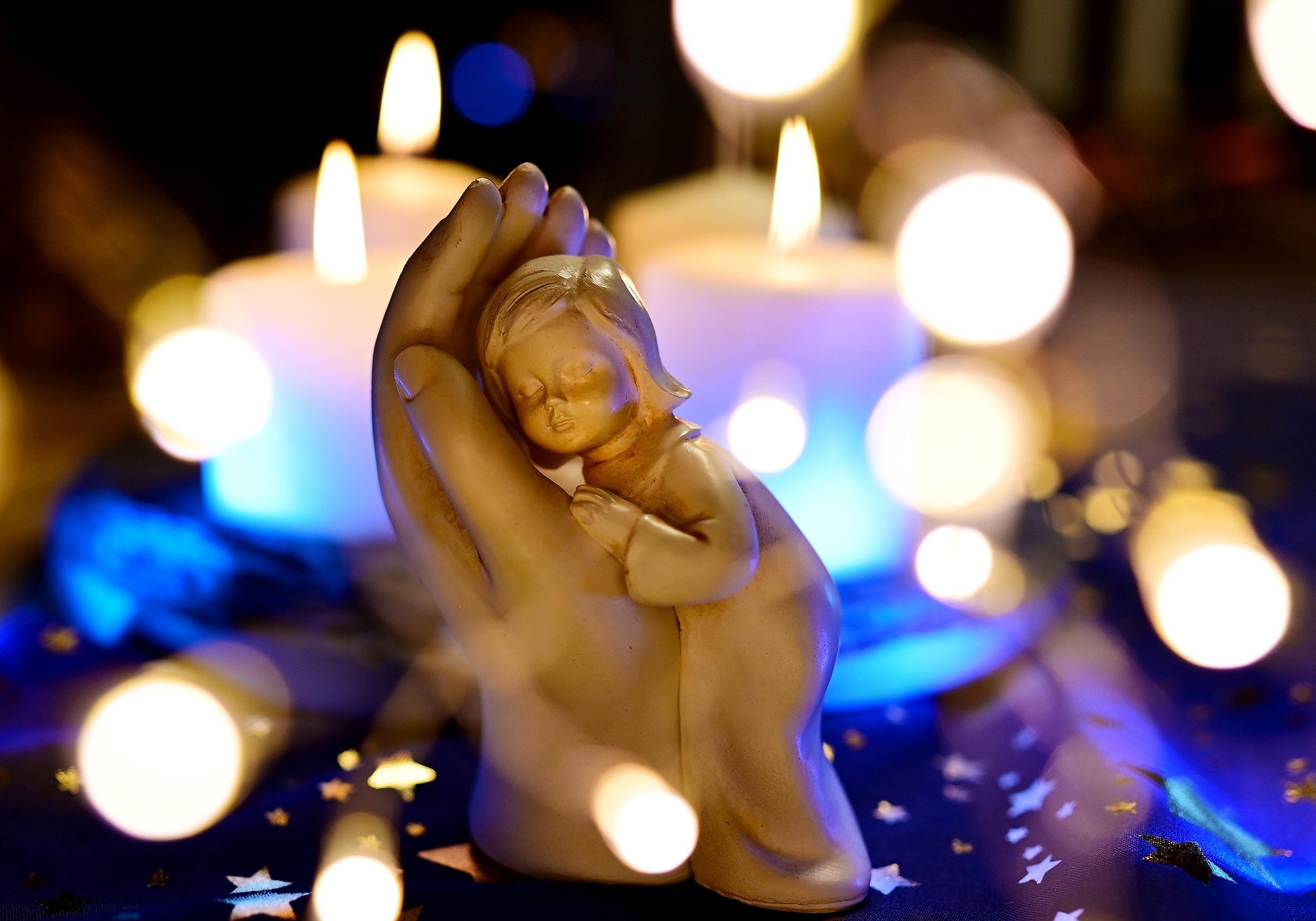 Holzfigur: Hand in der ein Kind sich einkuschelt, umgeben von Kerzenlichtern