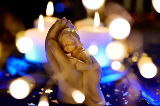 Holzfigur: Hand in der ein Kind sich einkuschelt, umgeben von Kerzenlichtern