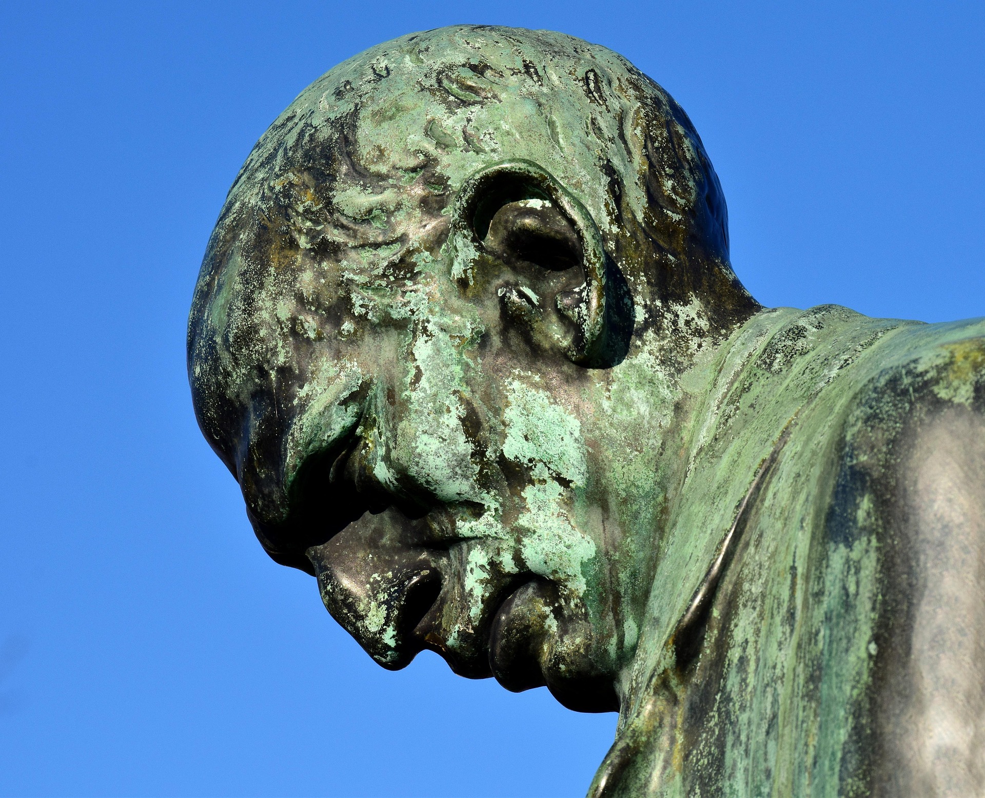 Kopf einer Bronzestatue mit viel Patina. Der Kopf ist geneigt, der Blick geht nach unten.