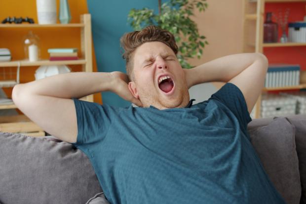 breit gähnender Mann mit Händern hinter dem Kopf auf einer Couch